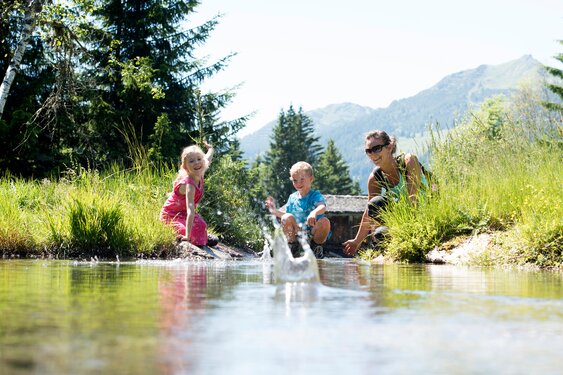 Playful moment at Silbisee in Silbertal – a young mother enjoys a summer’s day with her two small children at the lakeshore, surrounded by the nature of the Austrian Alps.