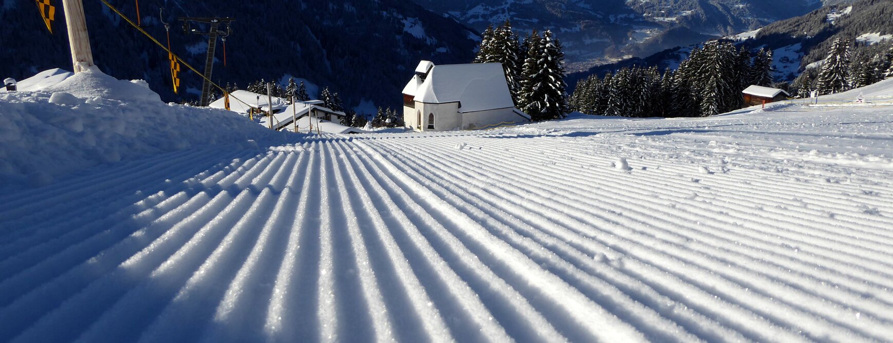 Perfekt präparierte Skipiste am Kristberg im Silbertal, dem Genießerberg im Montafon, mit verschneiter St. Agatha Kirche und Panoramablick auf das Verwall- und Rätikongebirge in den österreichischen Alpen. | © Montafoner Kristbergbahn Silbertal GmbH - Oliver Kern von skiresort.de