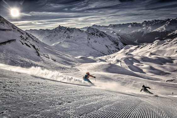 Perfectly groomed ski slope with two athletic skiers in Silvretta Montafon – the largest and most dynamic ski area in the Montafon Brandnertal region of the Austrian Alps.